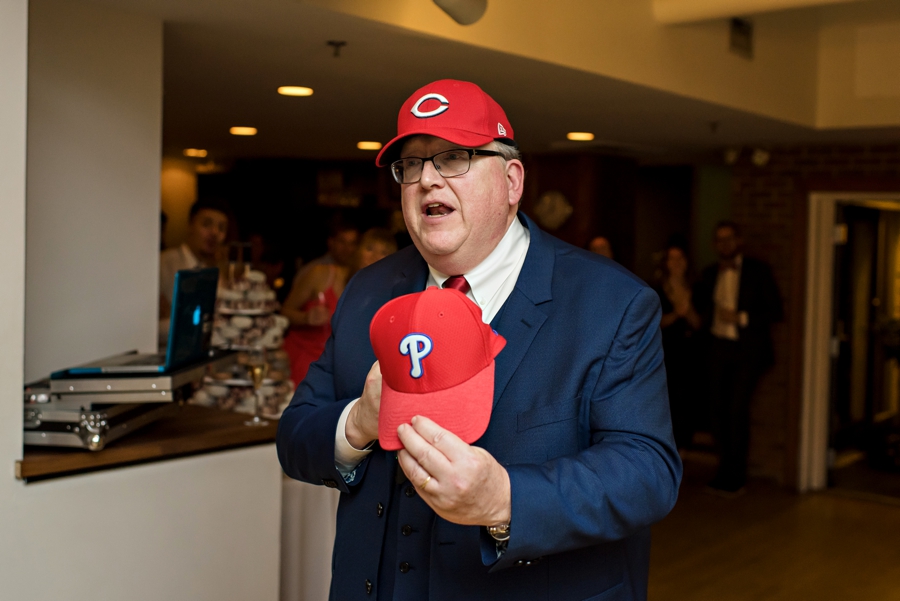 The father of the bride giving a speech with a Phillies hat in his hands.